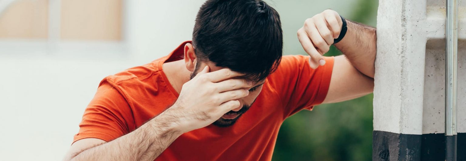 man resting elbow against wall and holing head to stop dizziness